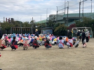 避難訓練の一環で見守りスタッフと児童が校庭に参集している様子